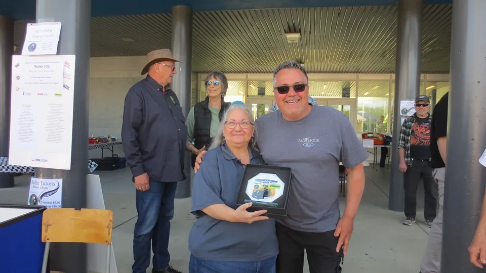 Tony Medonca, in a grey Ford Maverick t-shirt, stands beside a Fresh Co representative in a grey polo who holds the octagonal Country Car Show 2026 plaque, with a 50-50 draw poster to the left.